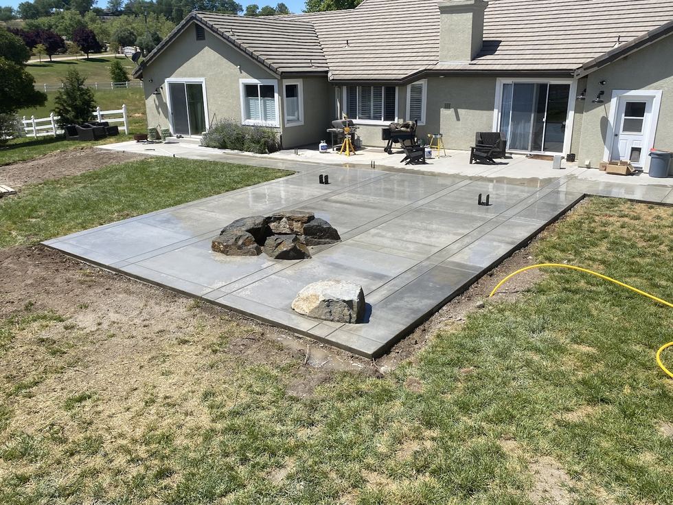 A freshly poured rear patio slab with a fire pit ring set into it, a house behind.