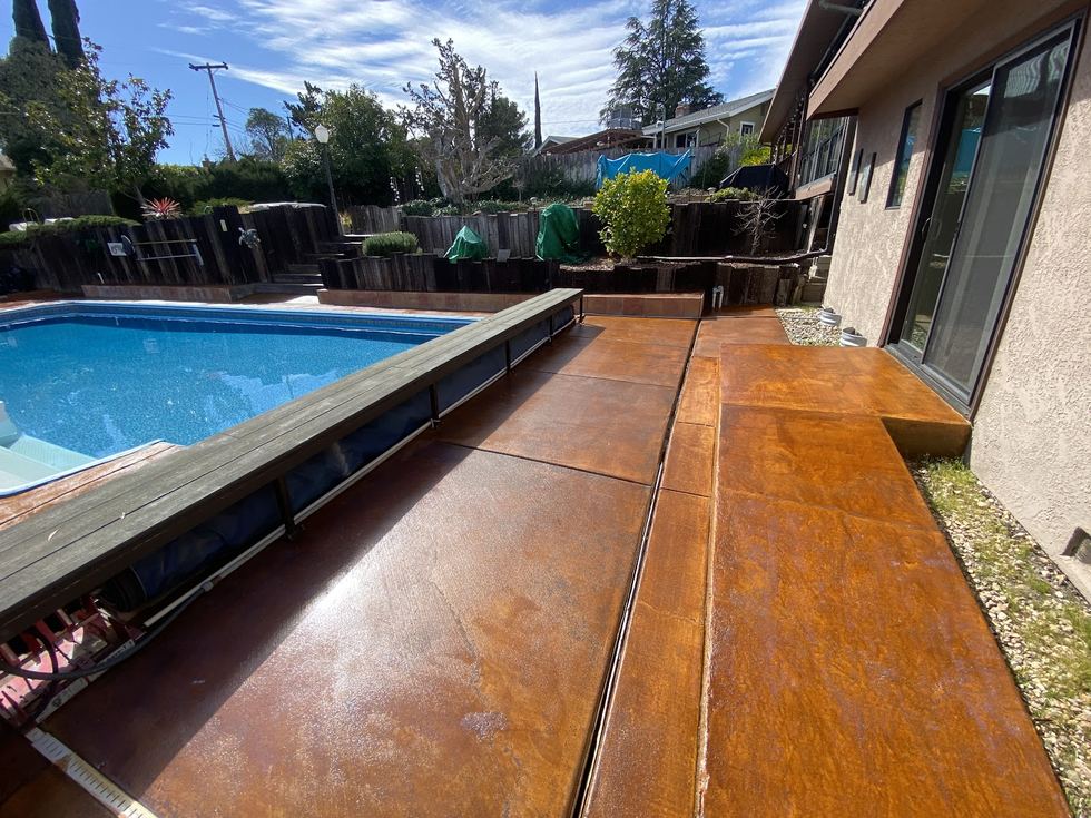 Stained concrete decking in a deep red-brown running along the edge of a swimming pool.