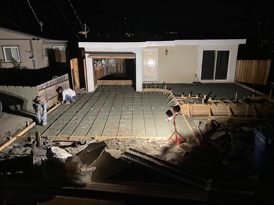 A site at night before a pour: timber forms laid out and a grid of steel reinforcing bar tied across the ground.